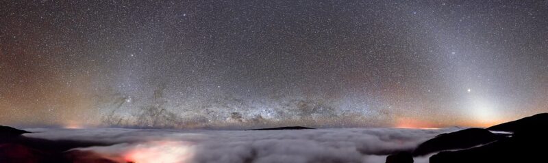 A panorama of the night sky with innumerable stars above a layer of clouds.