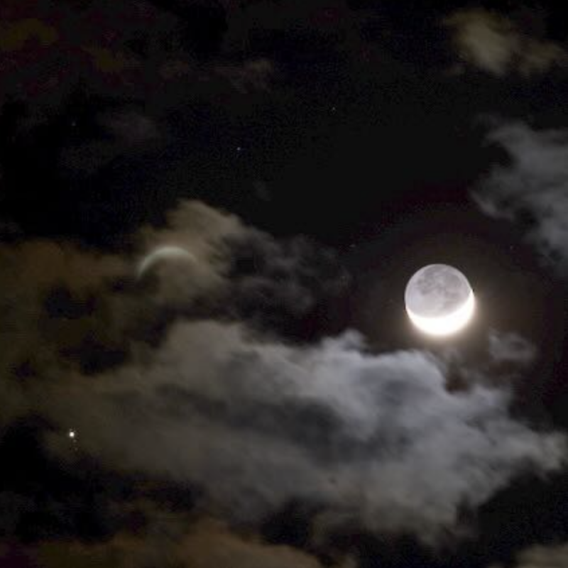 Bright crescent moon in broken clouds, with dots for Jupiter and its moons and a distant, fuzzy, faint crescent.