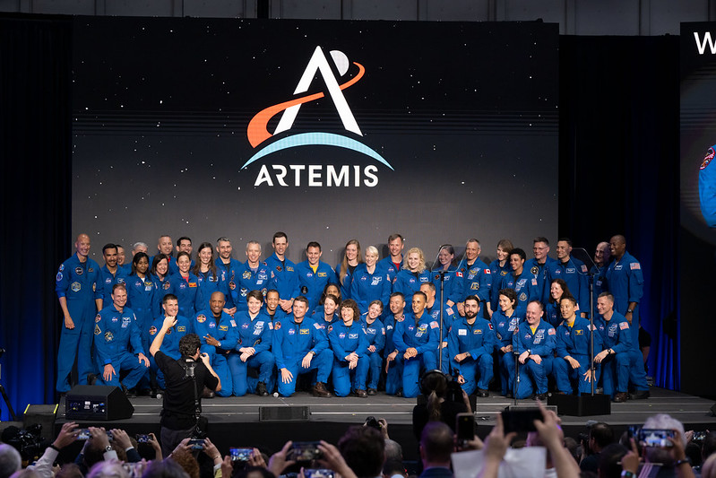 Be an astronaut: Many men and women in blue astronaut uniforms lined up for a group portrait under an Artemis logo.