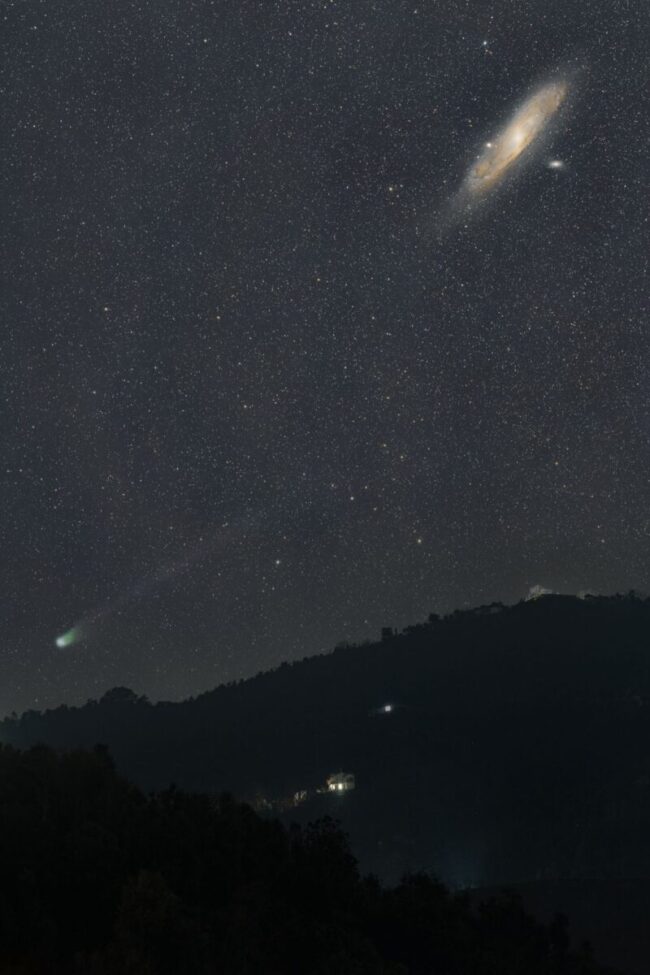 Bright dot with a faint tail undera a yellowish oblique disk. Mountains in the background and a starry dark sky.
