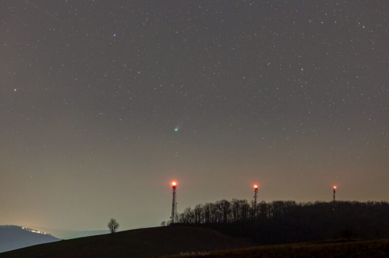 Dim, starry sky, three radio towers with red lights. A little green dot in the sky above them.