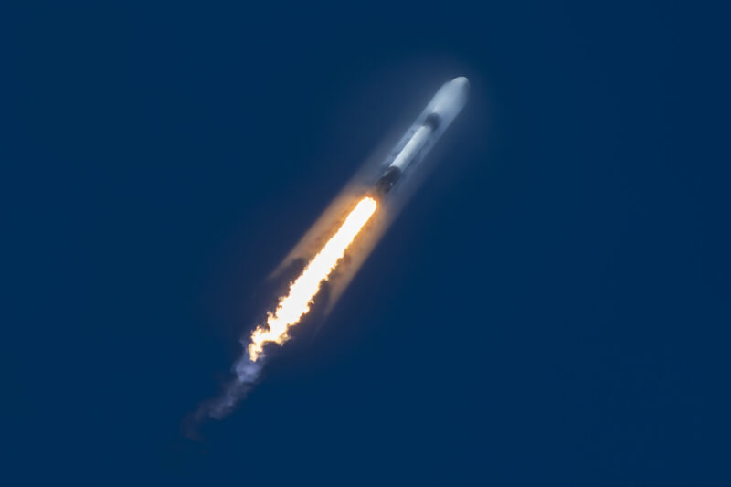 SpaceX Starlink: A rocket blasting through a deep blue sky with a jet of orange, yellow, and white propelling it upwards.