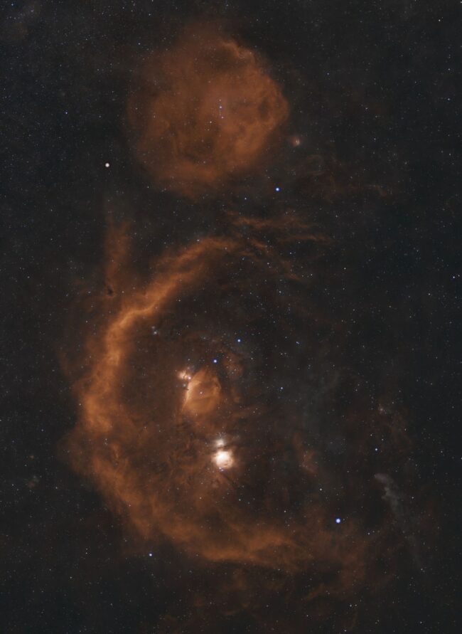 Two fuzzy and wispy orange space clouds, one round and the other a huge semicircle, among scattered stars.