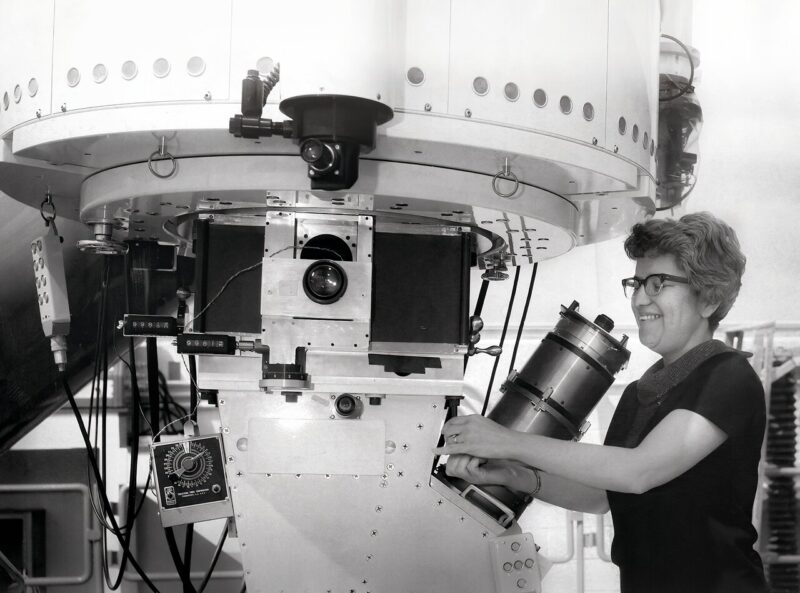 Black and white image of a woman with short hair using a big telescope.