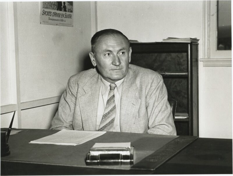 Black and white image of a man sitting in front of a desk.