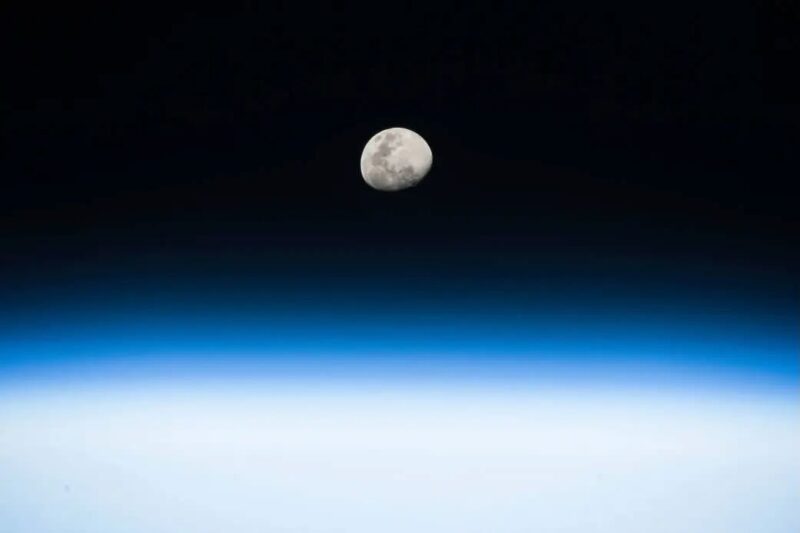 Almost round moon in black space above the curve of Earth.