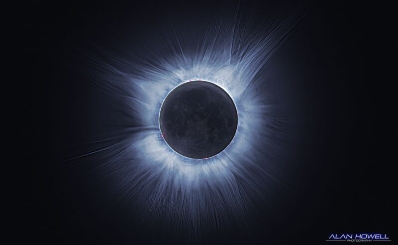 Image shows the totally eclipsed sun, visible as the black circle of the moon surrounded by the glowing, wispy corona of the sun with a deep purply-blue tint.