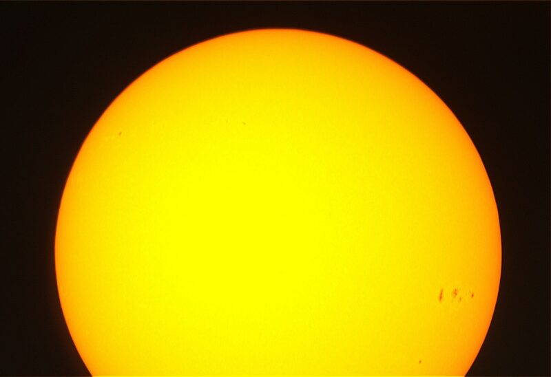 The sun, seen as a sectional yellow sphere with small dark spots.