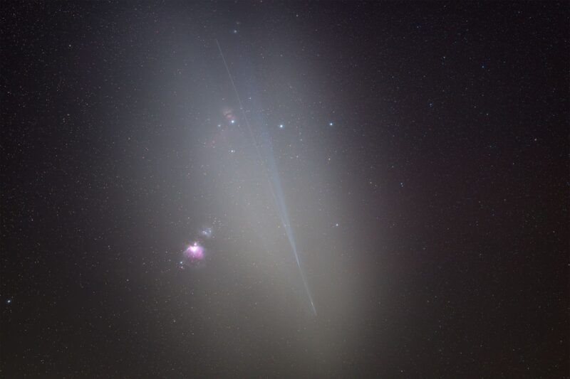 Small patches reddish nebulosity with a comet-like trail, over a background of distant stars.
