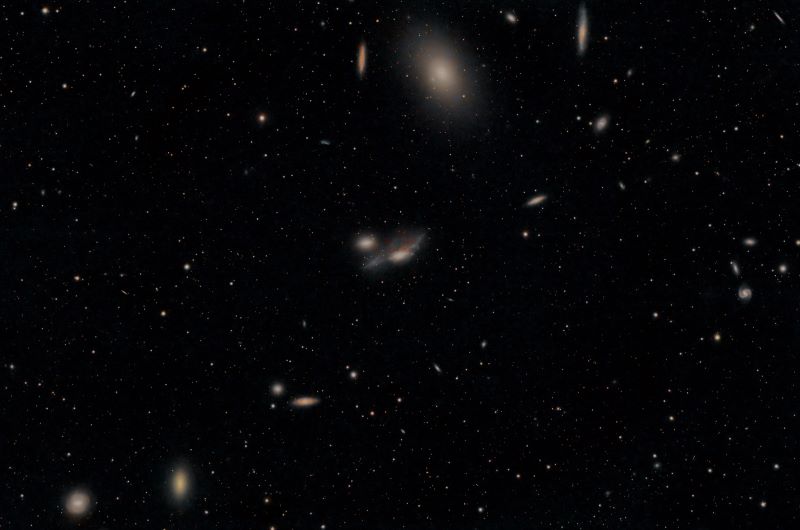 A chain of galaxies shown as lighter colored and fuzzy spots on a black background. All look orangish.
