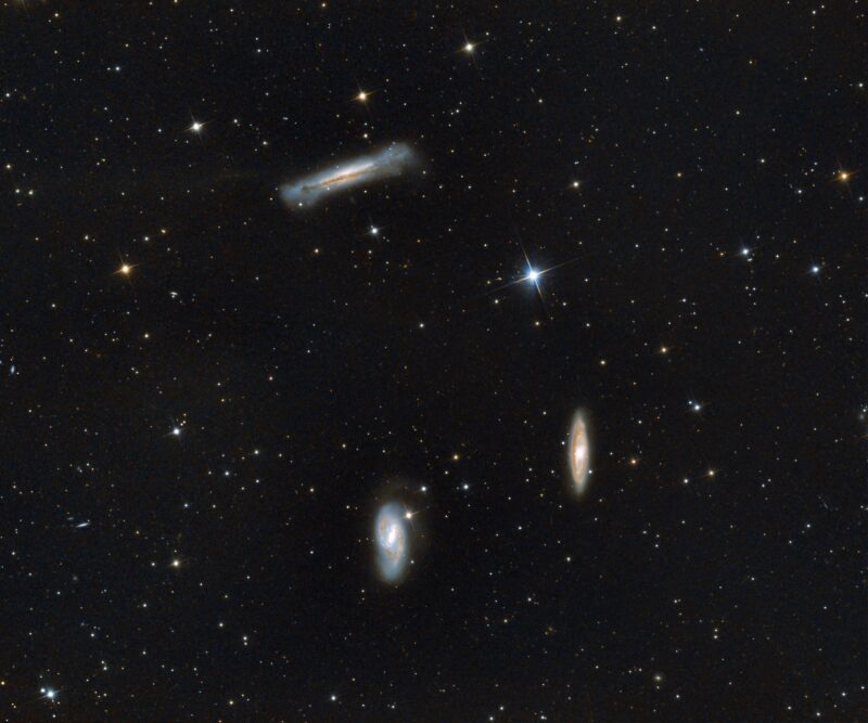 A trio of bright, whitish nebulous objects over a background of numerous stars.