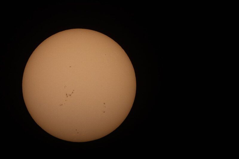 The sun, seen as a large yellowish sphere with small dark spots.