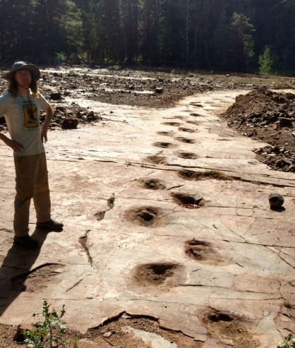 A man poses besides the dino tracks.