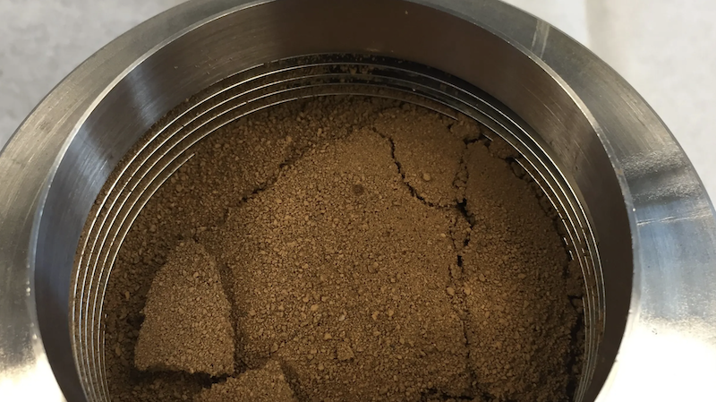 Clods of brownish soil-like material inside a round metallic container.