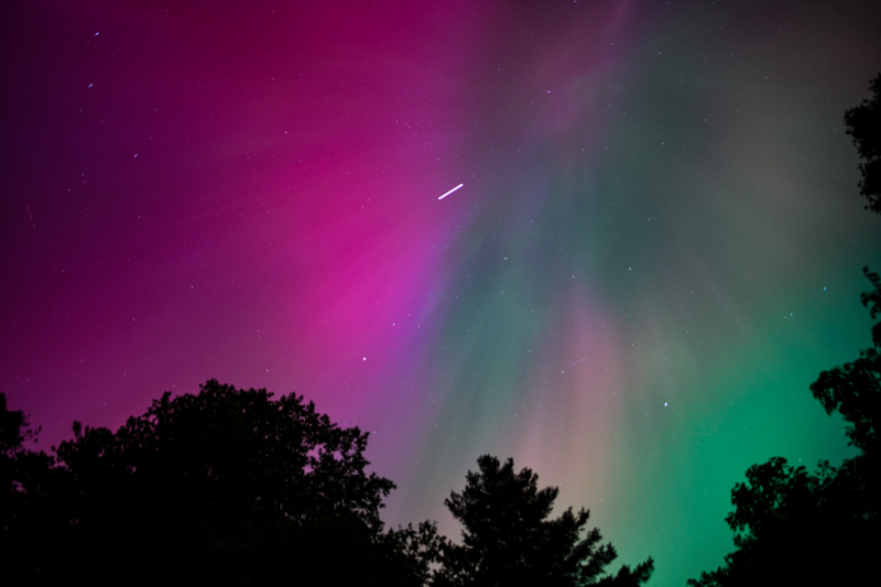 Brilliant red and green streaks of light in the sky, apparently descending from straight above toward the camera.