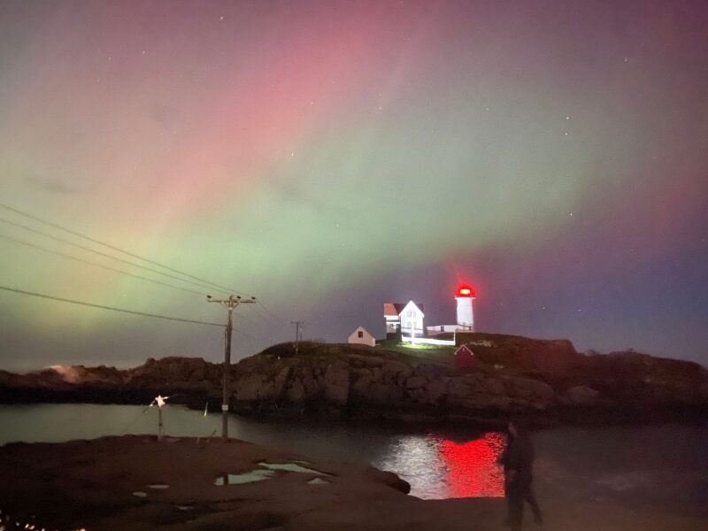 Fuzzy pink and green swaths of light over a well-lit distant lighthouse.