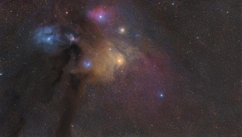 Large clouds of red, blue and yellow nebulosity over abundant background stars