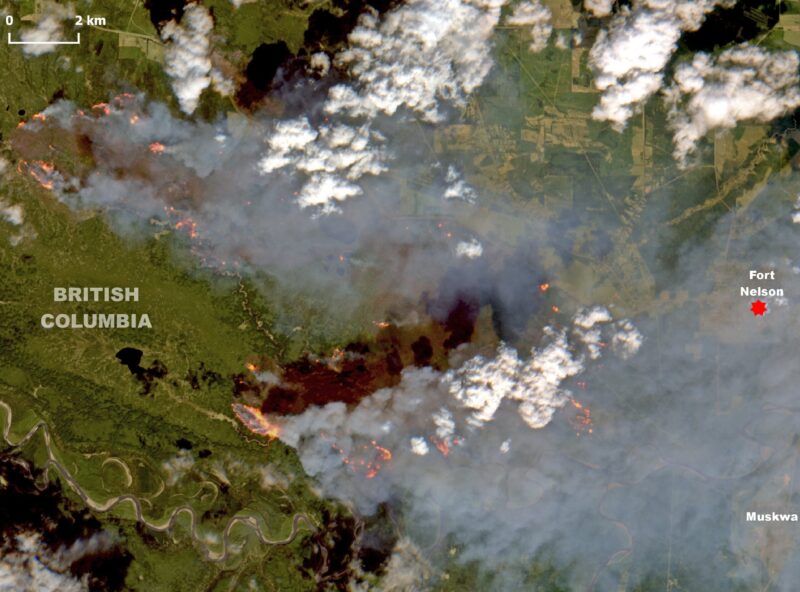 Satellite image of land below with labels for Canadian locations, orange spots for fires, gray smoke and white clouds.