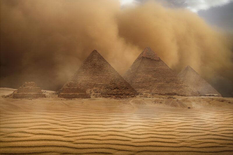 Egyptian pyramids: A desert with a sandstorm going on. There are 3 big pryamids in the center-right and 2 smaller ones on the left side.