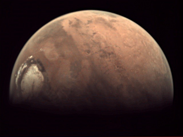 Part of Mars with its orangish surface and white polar cap against a black background.