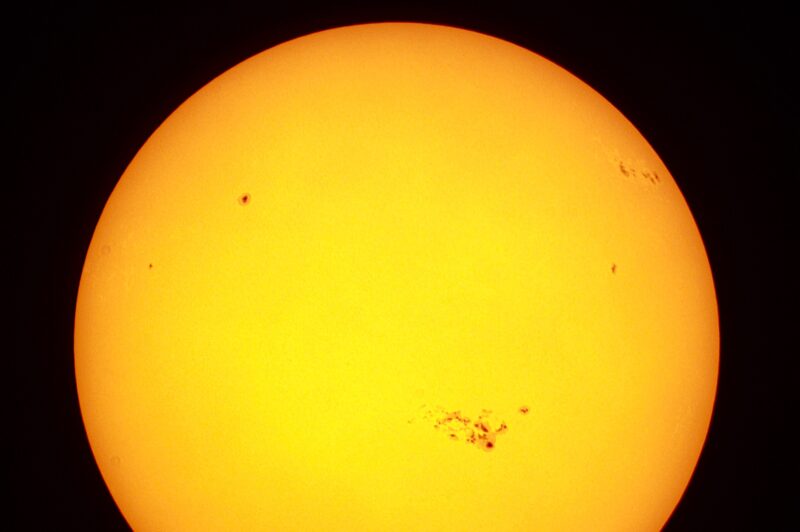 Yellowish sun with dark mottlings, including one near bottom right with lots of dark blotches.