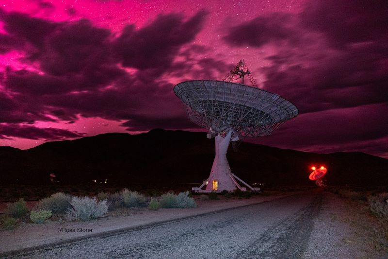 AI: A radio dish under a partly pink, starry and cloudy sky.