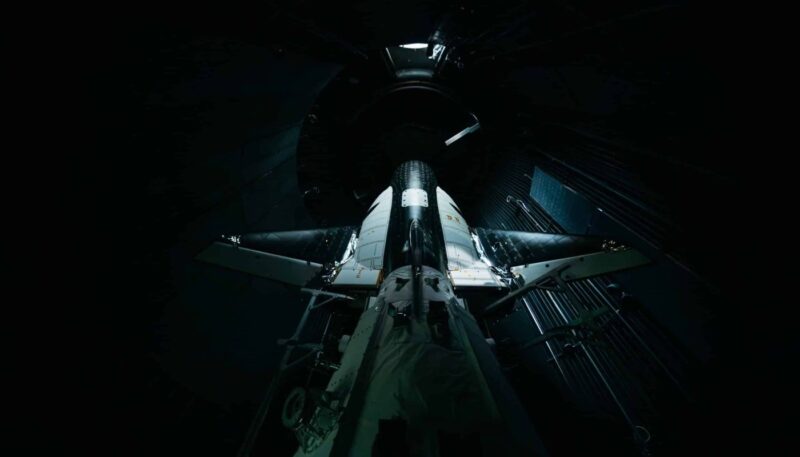 Black and white spaceplane mounted in testing bed inside a silo.