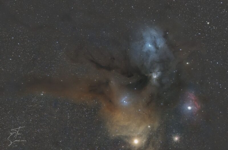 Large clouds of reddish, bluish and yellowish nebulosity over a multitude of background stars.