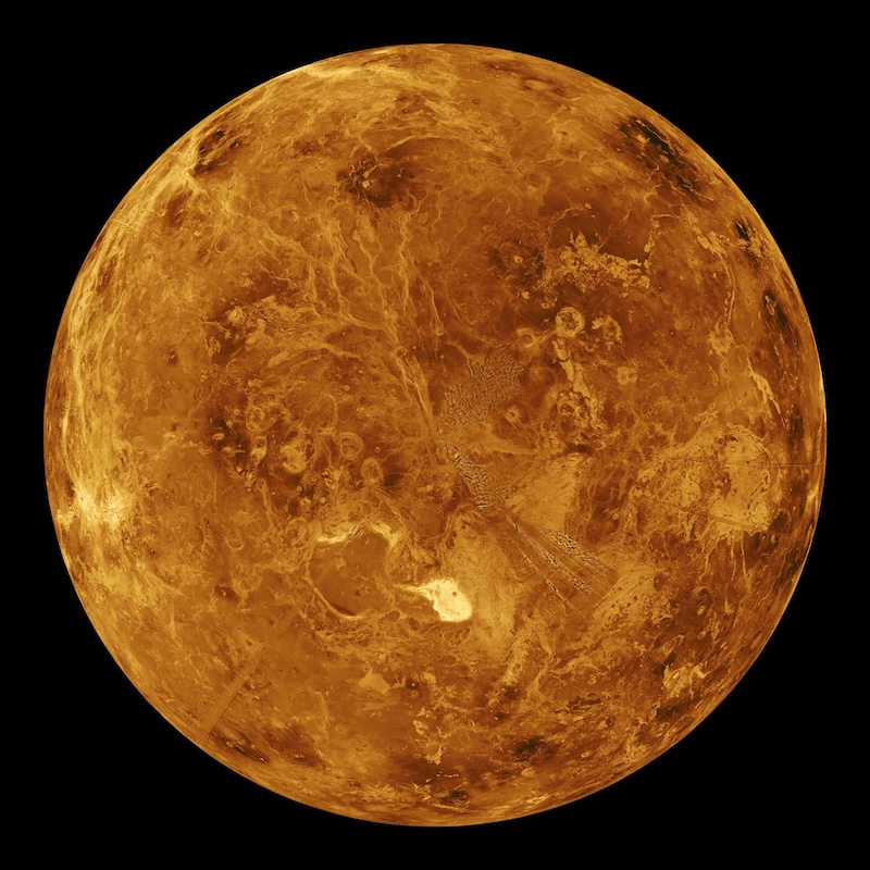 Orange-ish rocky planet with cracks and circular features on a mottled surface.