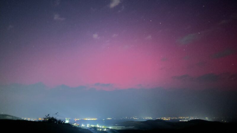 Layers of purple, pink, and blue paint the sky from top to bottom over a glowing city. A few bright dots scatter across the sky.