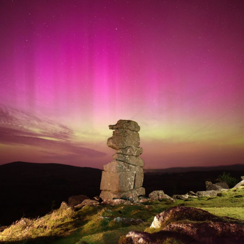 Sun news: Rock spire with pink and yellow auroral streamers behind.