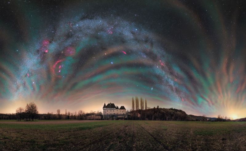A French chateau with an arching Milky Way and bands of iridescent colors stretching over top.