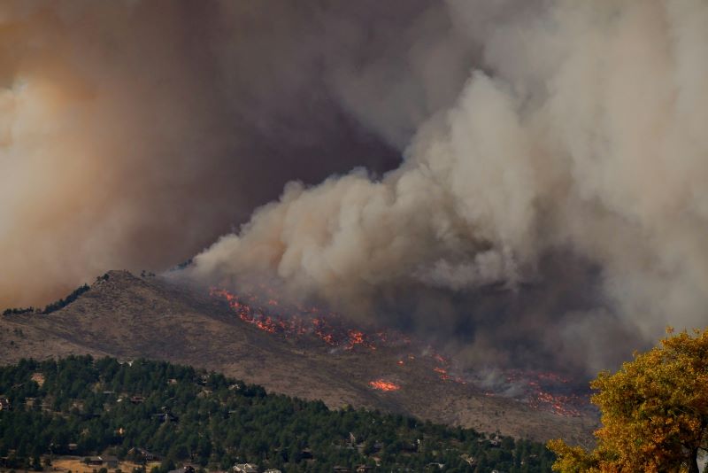 Wildfires: A mountainside on fire with dark billowing smoke filling the sky.