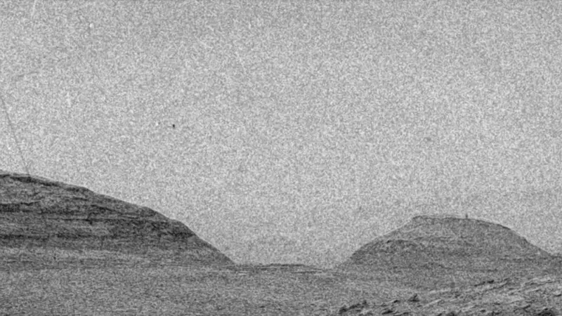 Gray hills under a lighter gray sky with particles and lines appearing and disappearing in the foreground.