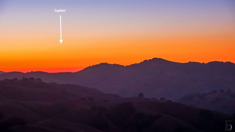 Orange sky with a white, small dot at the left side, over some mountains.