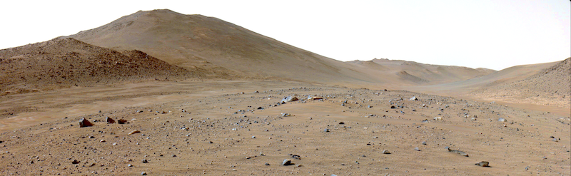 Terreno rocoso de color marrón con colinas a lo lejos y cielo blanco.