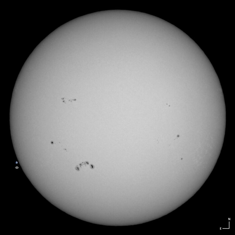 The sun, seen as a large white sphere with small dark spots.