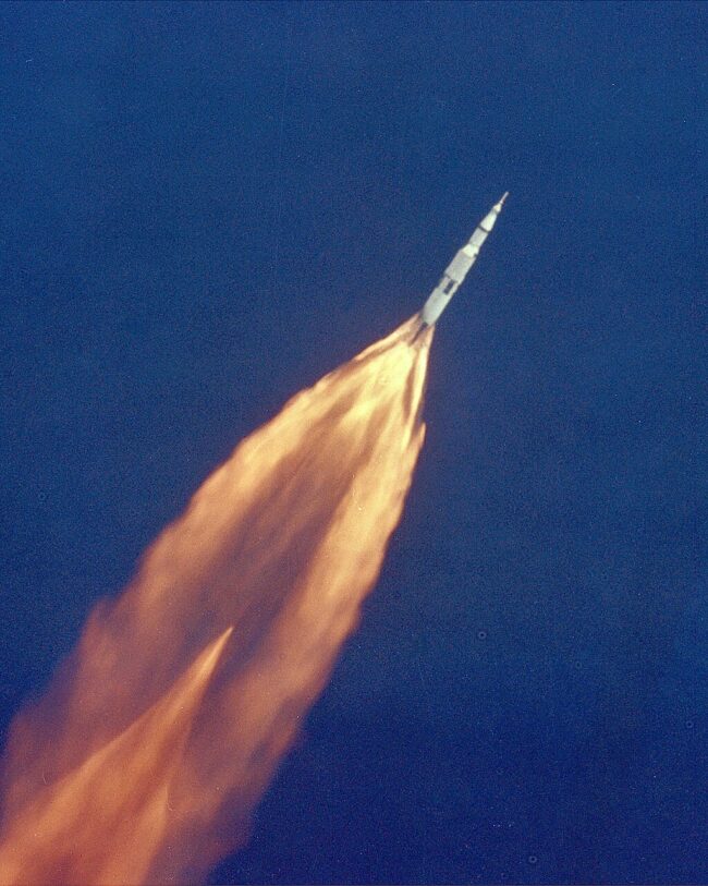 Distant ascending rocket with vast tail of orange flames.