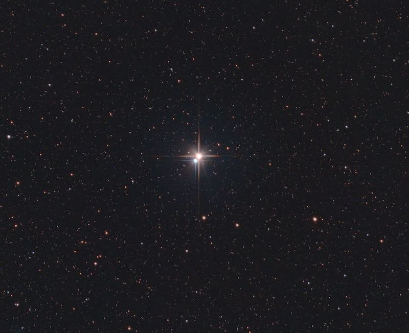A bright golden star and slightly smaller blue star very close together in the center of a field of stars.