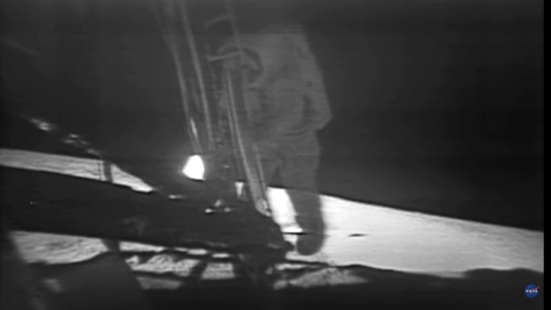 Fuzzy black and white photo of an astronaut stepping off ladder of the lunar lander.
