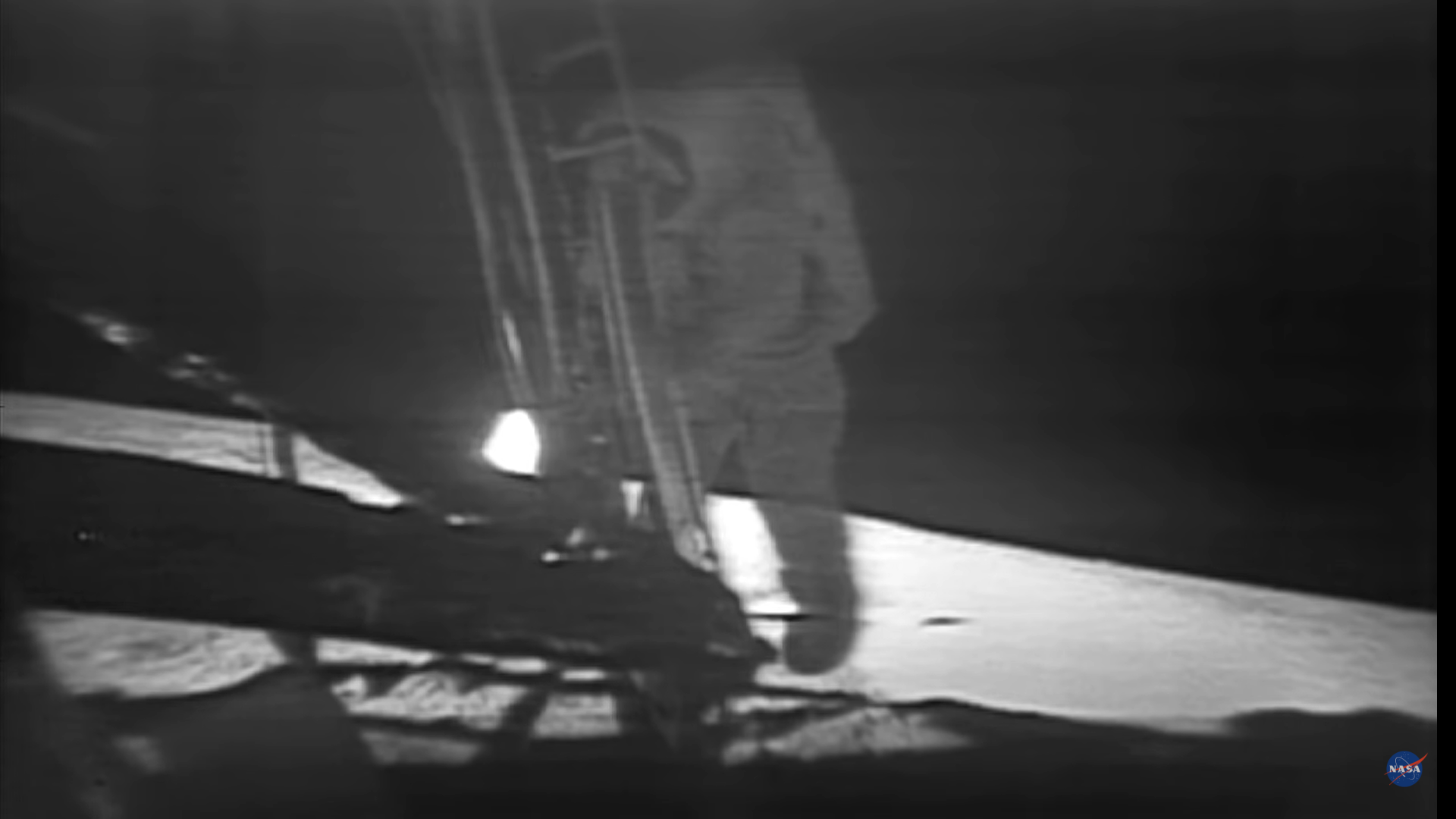 Fuzzy black and white photo of astronaut stepping off ladder of lunar lander.