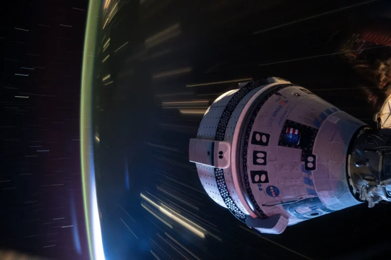 Starliner: Space capsule over colorful but indistinct landscape at night.