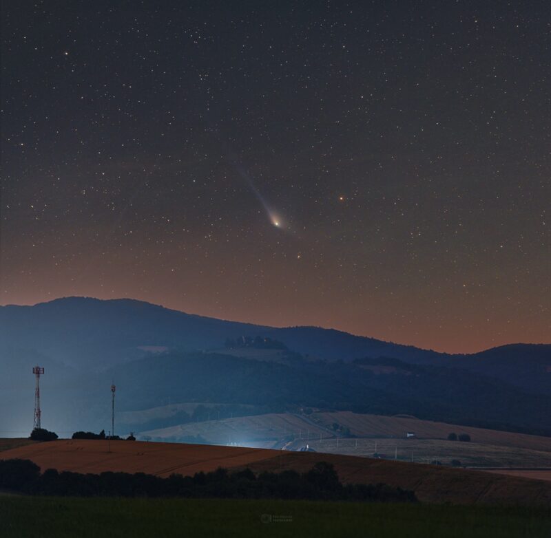 Dark landscape with a comet above showing 2 tails in different directions.