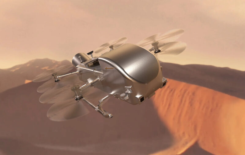 Drone-like machine with 8 rotors flying over reddish sand dunes under a reddish cloudy sky.