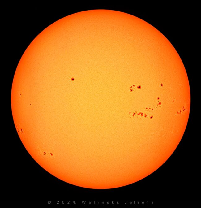 The sun, seen as a large yellow sphere with small dark spots.