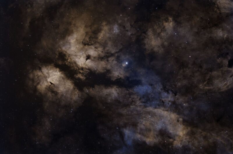 Large clouds of brownish-colored gas over a multitude of distant stars.