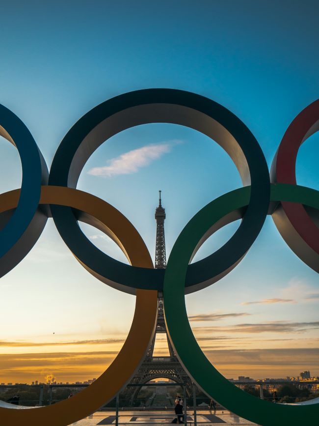 Summer Olympics: The Olympic rings with the Eiffel Tower seen through them at sunset.