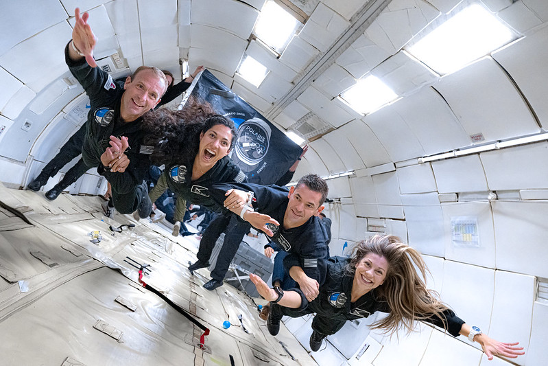 Two men and two women link arms inside a plane in zero gravity.