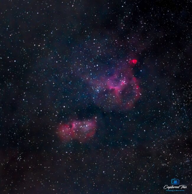 Two clouds of bright reddish nebulosity over a background of distant stars.