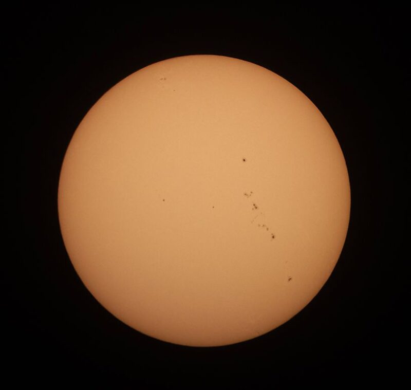 The sun, seen as a large yellowish sphere with small dark spots.